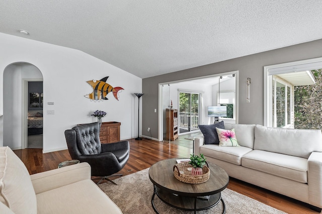 living room with lofted ceiling, arched walkways, wood finished floors, and a textured ceiling