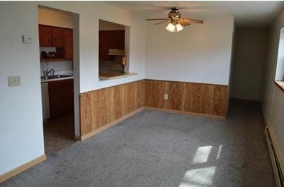 7673 River Rd, Fridley, MN 55432 - spare room featuring a baseboard radiator, a ceiling fan, wainscoting, wooden walls, and carpet flooring