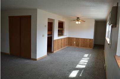 7673 River Rd, Fridley, MN 55432 - unfurnished living room featuring a ceiling fan, a wainscoted wall, carpet flooring, and wood walls