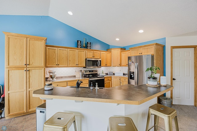 kitchen featuring appliances with stainless steel finishes, vaulted ceiling, a breakfast bar area, tasteful backsplash, and dark countertops