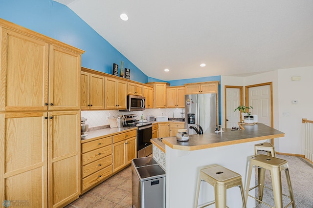 kitchen with appliances with stainless steel finishes, lofted ceiling, a kitchen breakfast bar, tasteful backsplash, and a kitchen island with sink