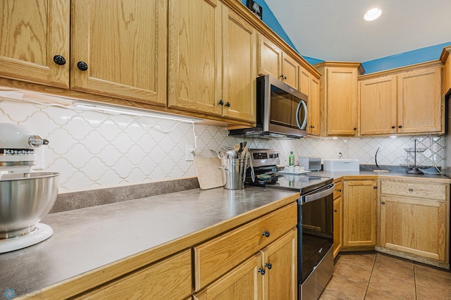 kitchen featuring appliances with stainless steel finishes, tasteful backsplash, light tile patterned floors, and dark countertops