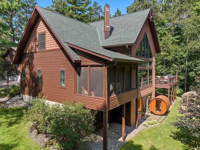 26746 County Road 4, Nisswa, MN 56468 - view of side of property featuring a chimney, a sunroom, a shingled roof, a lawn, and a deck