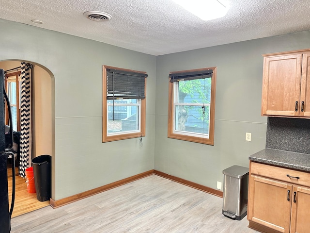 1429 Circle Dr, Albert Lea, MN 56007 - unfurnished dining area with light wood-style floors, arched walkways, a textured ceiling, and baseboards