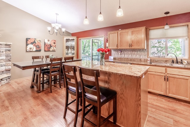 kitchen with a sink, lofted ceiling, a center island, light brown cabinets, and light wood-type flooring