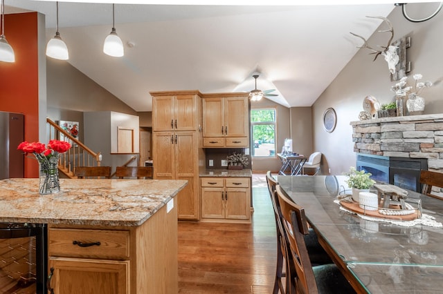kitchen featuring beverage cooler, vaulted ceiling, light wood-style flooring, a ceiling fan, and a stone fireplace