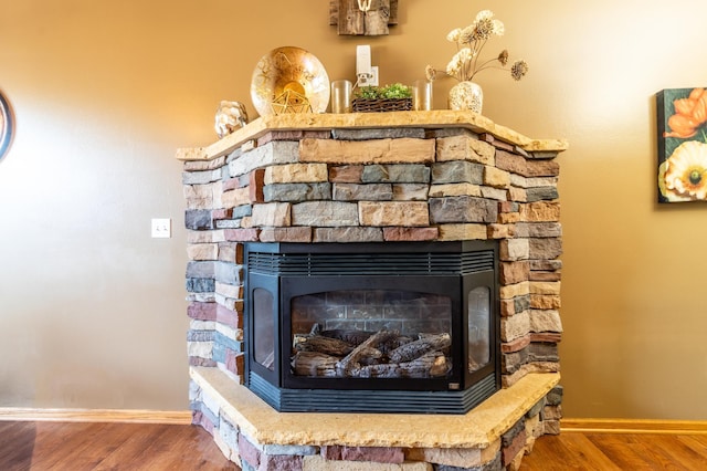 detailed view of wood finished floors, baseboards, and a stone fireplace