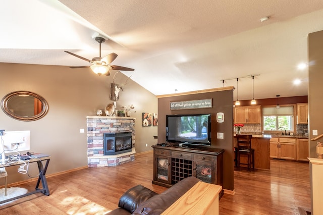 living area featuring ceiling fan, a fireplace, light wood-type flooring, vaulted ceiling, and baseboards