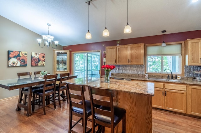 kitchen featuring a sink, lofted ceiling, decorative backsplash, light wood-style flooring, and a kitchen island