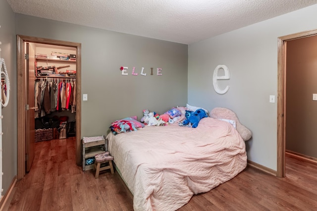 bedroom featuring a walk in closet, wood finished floors, a closet, and baseboards
