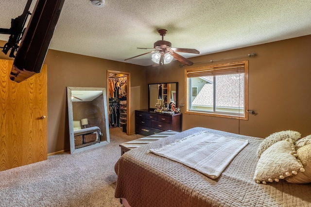 carpeted bedroom with a walk in closet, a closet, a ceiling fan, and a textured ceiling