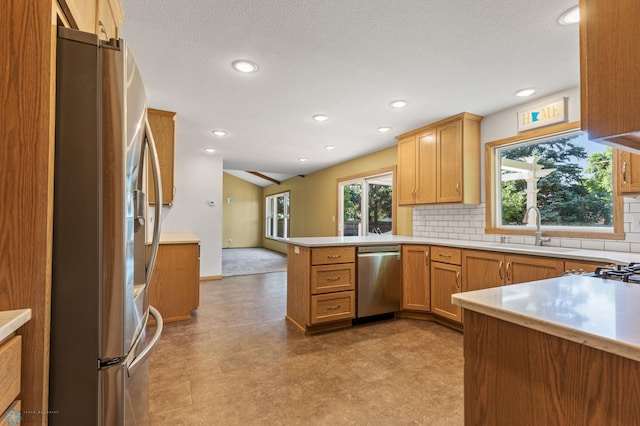 kitchen with stainless steel appliances, a sink, a peninsula, light floors, and backsplash
