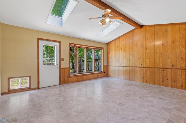empty room with a skylight, wood walls, a wainscoted wall, and ceiling fan