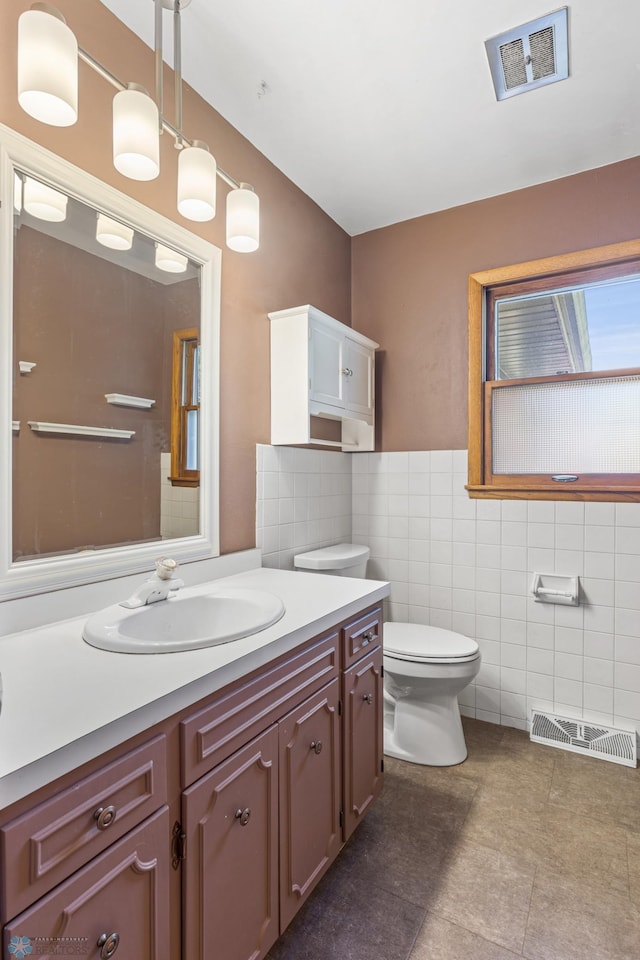 bathroom featuring tile walls, toilet, vanity, tile patterned flooring, and a wainscoted wall