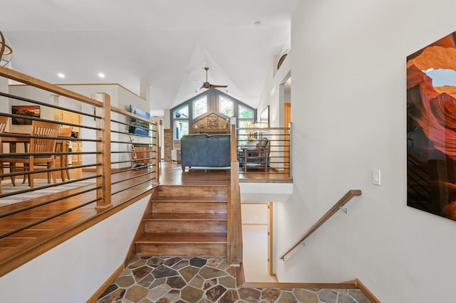 stairs with a ceiling fan, stone finish flooring, and high vaulted ceiling
