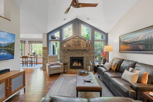 living room featuring wood finished floors, a stone fireplace, a ceiling fan, and high vaulted ceiling