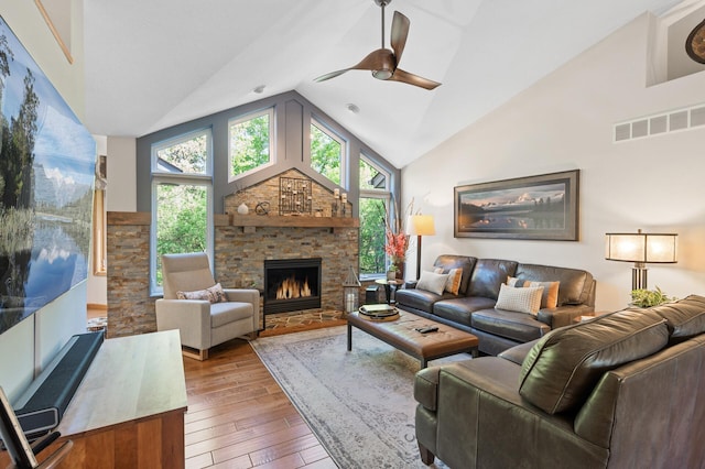 living room featuring hardwood / wood-style floors, a ceiling fan, a stone fireplace, and high vaulted ceiling