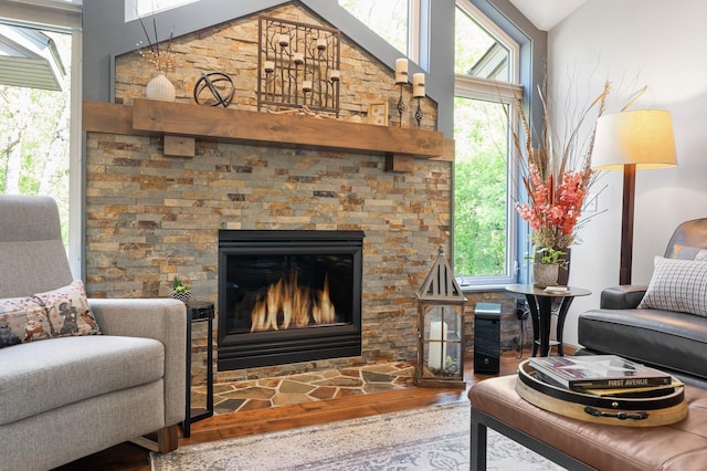 living room with wood finished floors, vaulted ceiling, healthy amount of natural light, and a stone fireplace