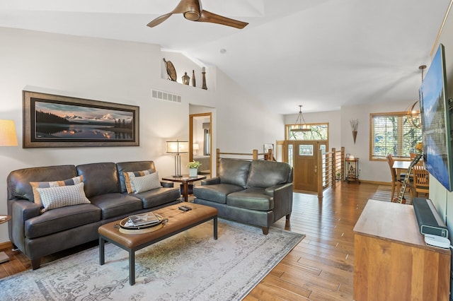 living area with vaulted ceiling, light wood-style floors, a ceiling fan, baseboards, and a chandelier