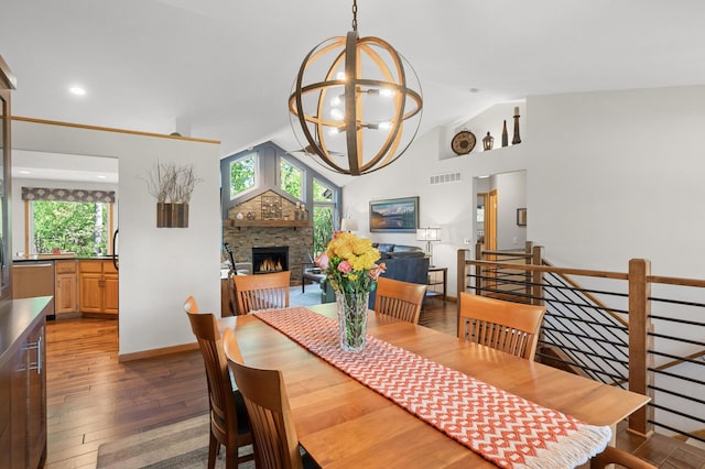 dining area featuring a chandelier, plenty of natural light, hardwood / wood-style flooring, vaulted ceiling, and a lit fireplace