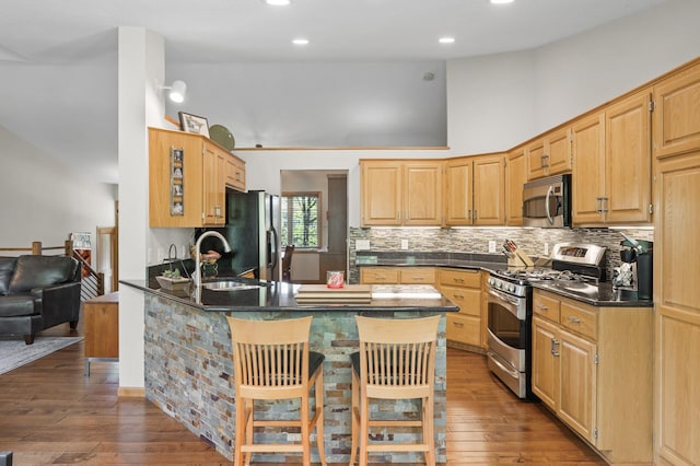 kitchen featuring stainless steel appliances, dark countertops, a peninsula, a sink, and decorative backsplash