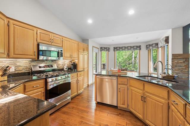 kitchen featuring appliances with stainless steel finishes, a sink, decorative backsplash, dark stone countertops, and light wood finished floors