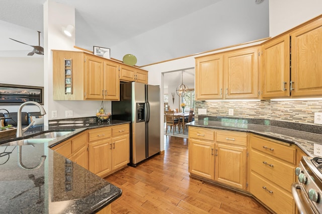 kitchen with stainless steel appliances, a sink, light wood-style floors, dark stone countertops, and decorative backsplash
