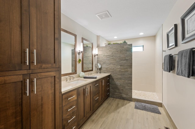 bathroom featuring wood finished floors, a walk in shower, and double vanity