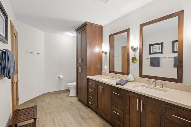 full bathroom with toilet, wood finished floors, double vanity, and baseboards