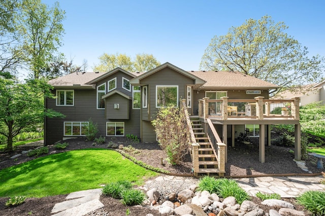 rear view of house with stairs, a wooden deck, a yard, and roof with shingles