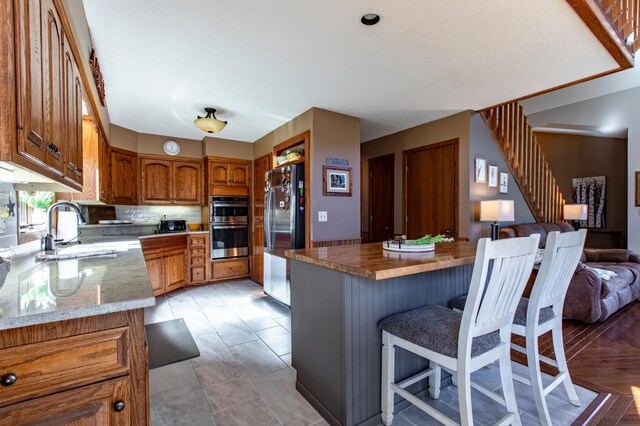 6385 13th Ave NW, Rochester, MN 55901 - kitchen featuring stainless steel appliances, a sink, brown cabinetry, open floor plan, and a breakfast bar area