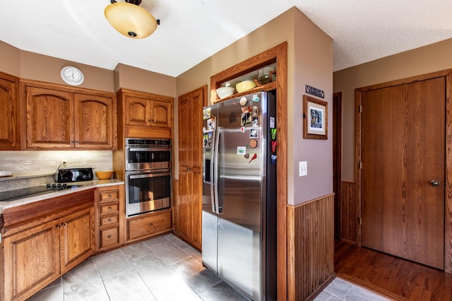 6385 13th Ave NW, Rochester, MN 55901 - kitchen with stainless steel appliances, brown cabinetry, wainscoting, light countertops, and tasteful backsplash