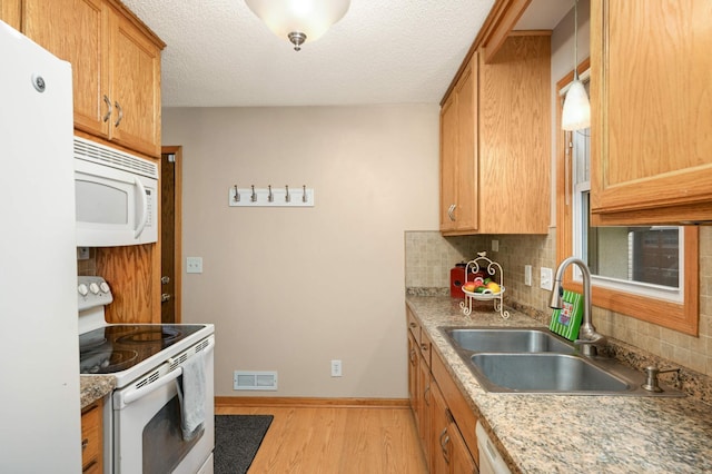 kitchen featuring white appliances, a sink, backsplash, light wood-type flooring, and baseboards