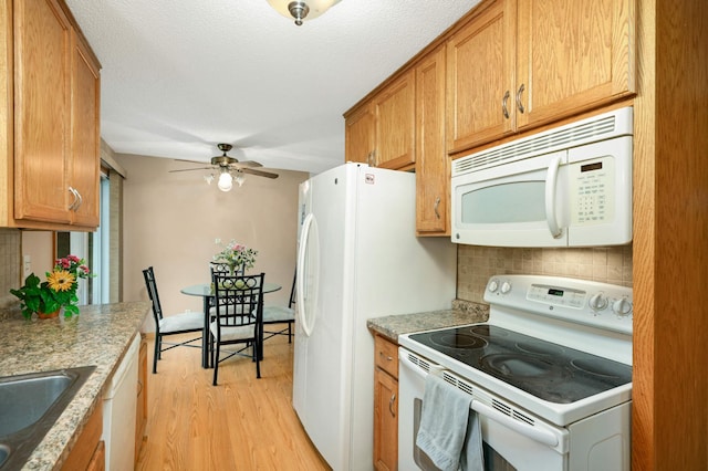 kitchen with white appliances, decorative backsplash, light wood-type flooring, a sink, and brown cabinetry