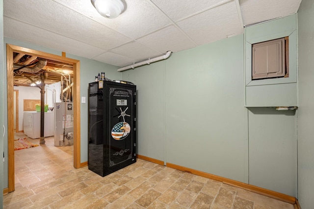 finished below grade area with water heater, baseboards, stacked washer / drying machine, and a drop ceiling