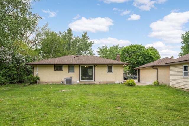 back of house featuring central air condition unit, a chimney, stucco siding, and a lawn