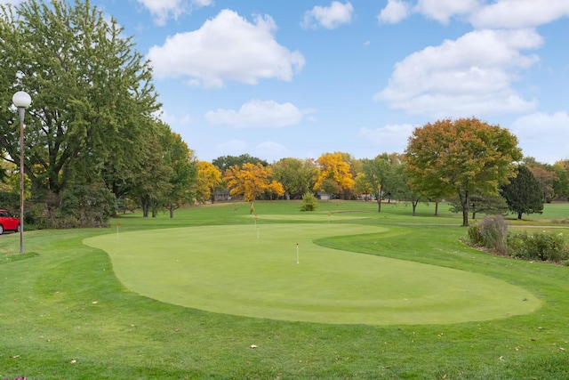 view of home's community with a putting green, view of wooded area, view of golf course, and a lawn