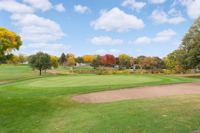 surrounding community featuring a putting area, a yard, view of golf course, and view of wooded area