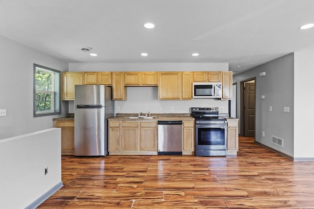 kitchen with appliances with stainless steel finishes, recessed lighting, wood finished floors, a sink, and light brown cabinetry