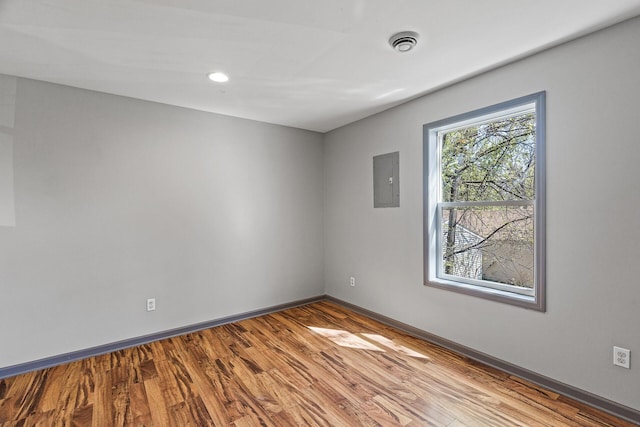 empty room with wood finished floors, baseboards, and electric panel