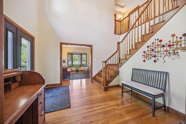 entrance foyer featuring light wood-style floors, plenty of natural light, a towering ceiling, stairs, and baseboards