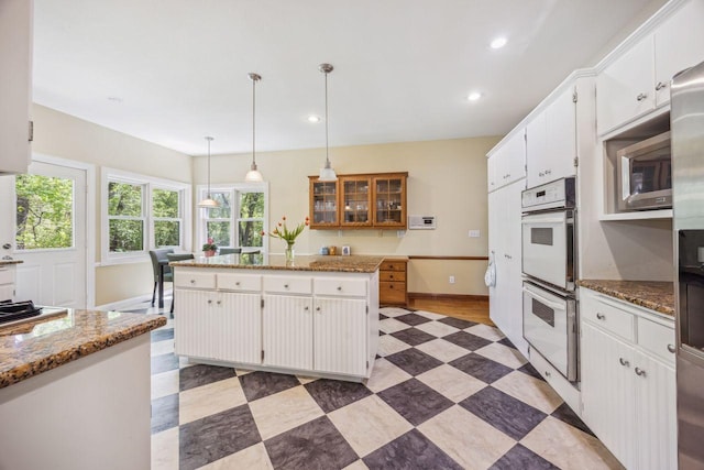 kitchen with white double oven, a kitchen island, stainless steel microwave, white cabinetry, and recessed lighting
