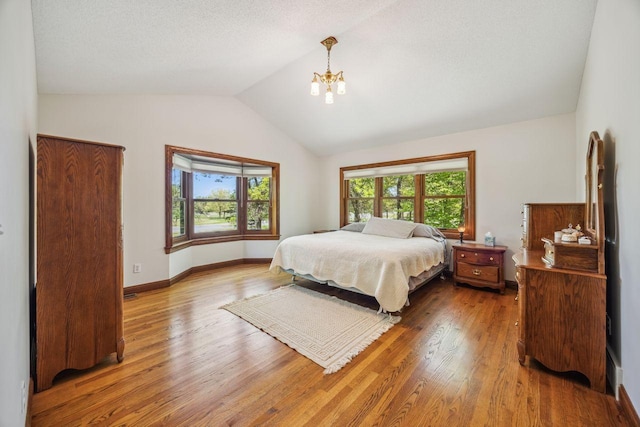 bedroom with a chandelier, lofted ceiling, wood finished floors, and baseboards