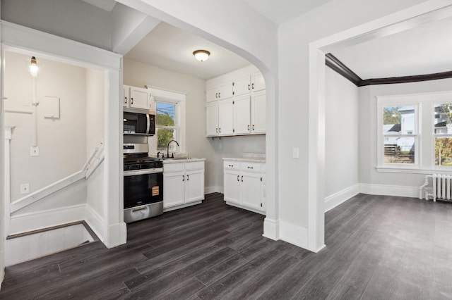 kitchen featuring appliances with stainless steel finishes, radiator heating unit, white cabinetry, and dark wood finished floors