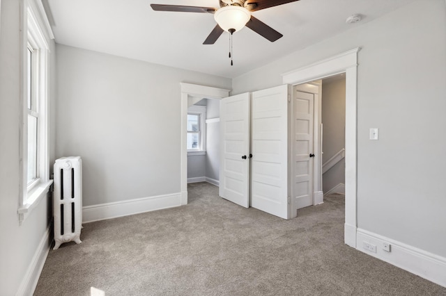 unfurnished bedroom featuring radiator heating unit, carpet, ceiling fan, and baseboards