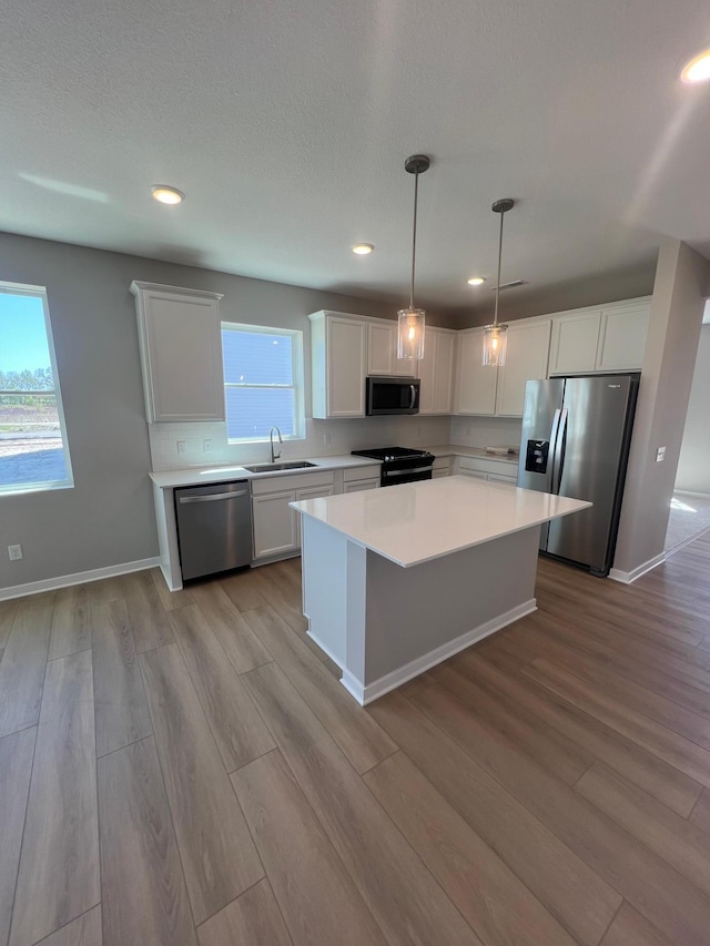 12515 Erskin St NE, Blaine, MN 55449 - kitchen with stainless steel appliances, a kitchen island, white cabinets, light countertops, and wood finished floors