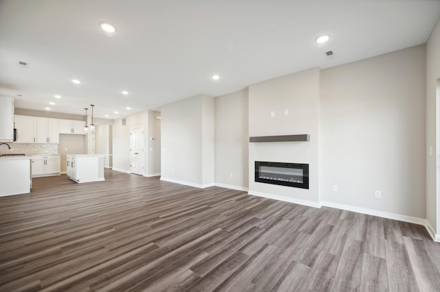 12515 Erskin St NE, Blaine, MN 55449 - unfurnished living room with wood finished floors, recessed lighting, baseboards, a glass covered fireplace, and a sink