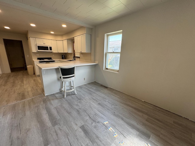 709 Center St E, Roseau, MN 56751 - kitchen featuring white appliances, light wood-style flooring, light countertops, a peninsula, and white cabinetry