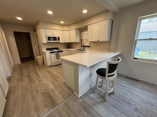 709 Center St E, Roseau, MN 56751 - kitchen featuring white appliances, a sink, light wood-style floors, a peninsula, and white cabinets