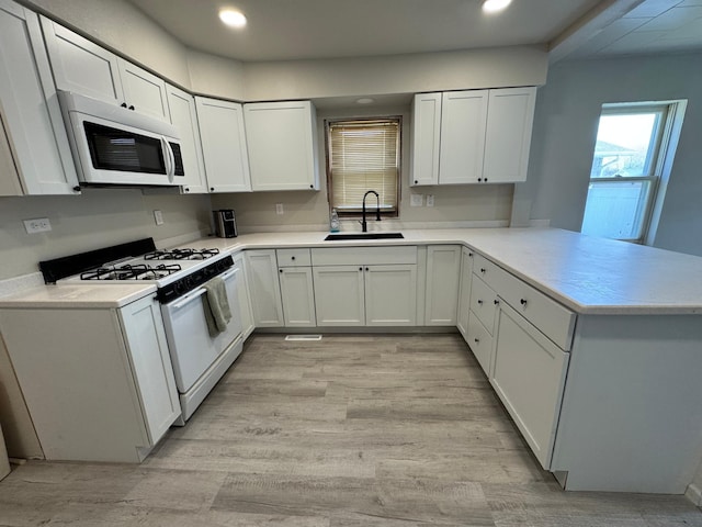 709 Center St E, Roseau, MN 56751 - kitchen with range with gas cooktop, white microwave, a sink, a peninsula, and light wood-style floors